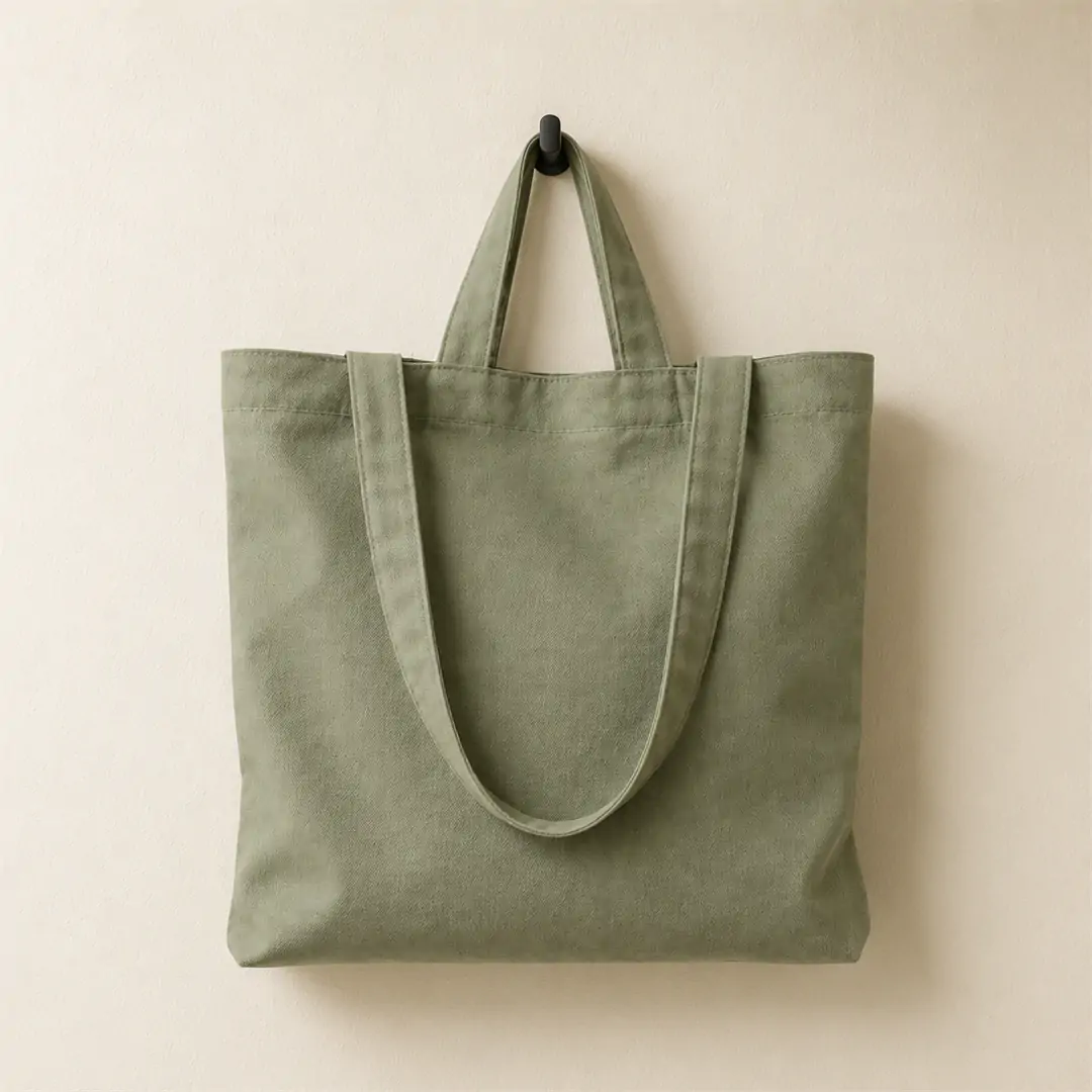 Sage green cotton tote bag 38x38cm with dual handles — short top handles and long shoulder straps — hanging on a wall hook