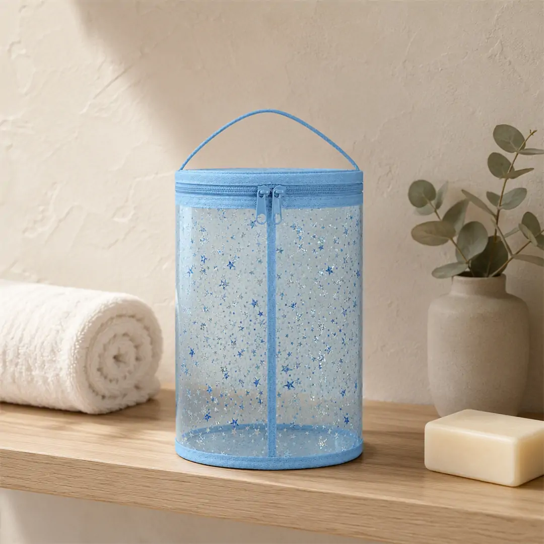 Clear PVC cylinder toiletry bag 9.5 x 6 x 4 in with pink binding, silver and pink star print and a double-slider top zip, shown on a white background with dimension marks