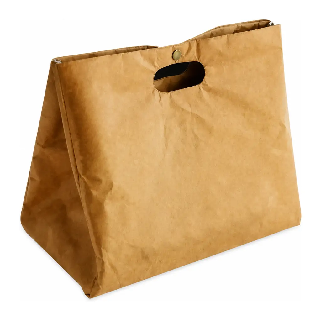 Kraft paper cooler bag with a built-in die-cut handle held under a running tap, with water beading on its water-resistant surface above a stainless steel sink
